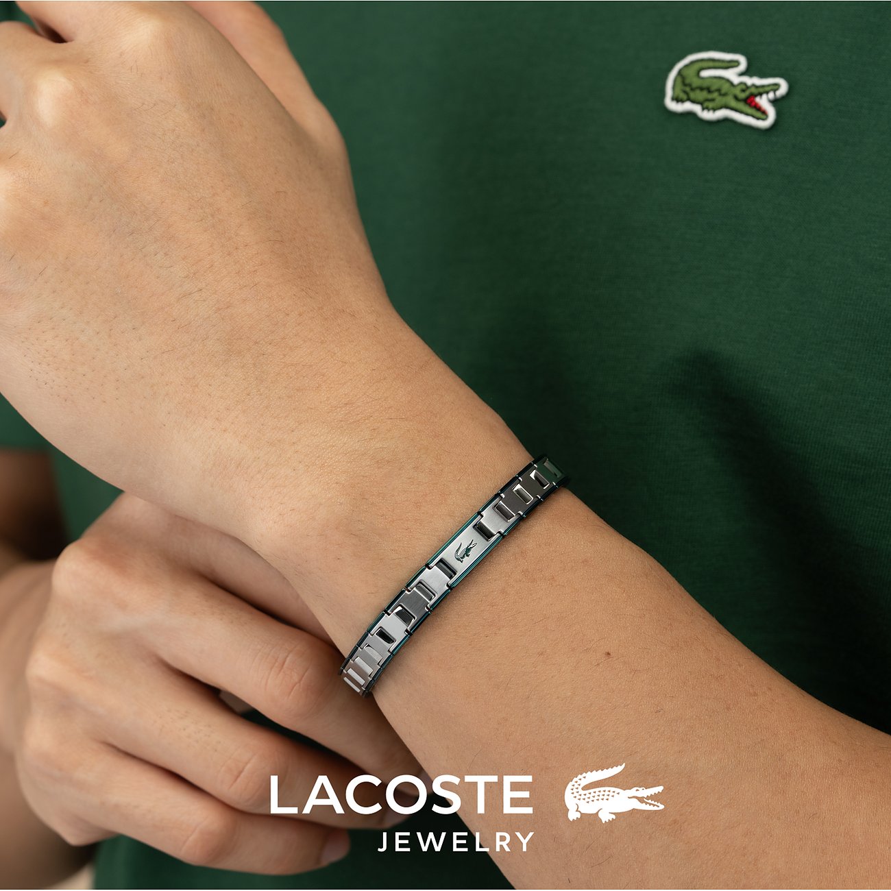 Een Lacoste armband van roestvrij staal, gedragen om een pols, met het krokodillenlogo op het middendeel.