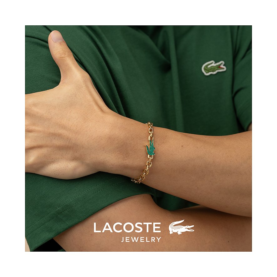 Am Handgelenk eines Models getragenes goldenes Lacoste Armband aus Edelstahl mit Krokodillogo aus grünem Kristall.