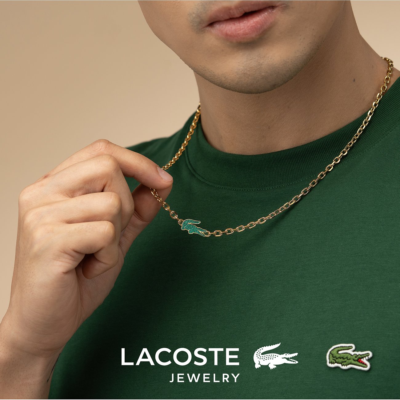 Nahaufnahme eines Mannes, der eine goldfarbene Lacoste Edelstahl-Halskette mit einem grünen Krokodil-Anhänger trägt.